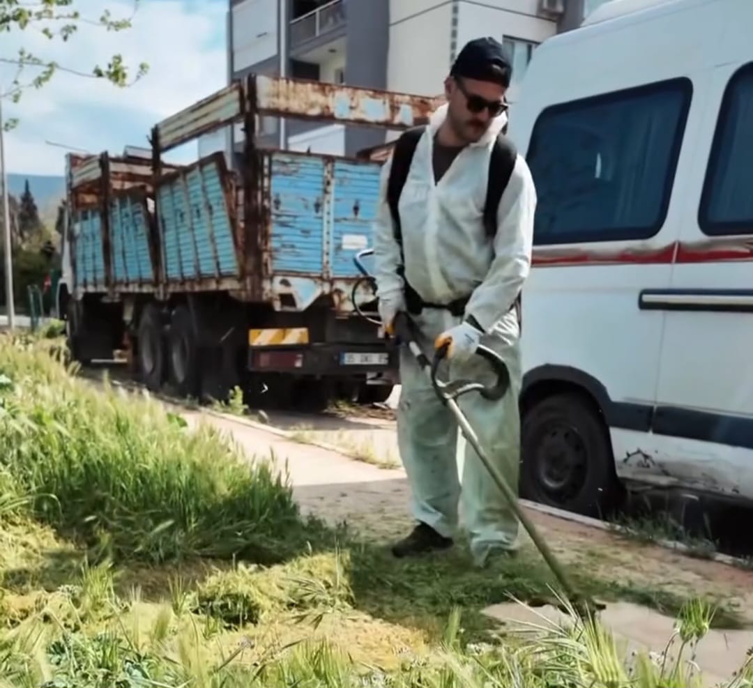 Çiğli Belediyesi temizlik personeli koruyucu kıyafetlerle mahalle aralarında ot biçme çalışması yapıyor.