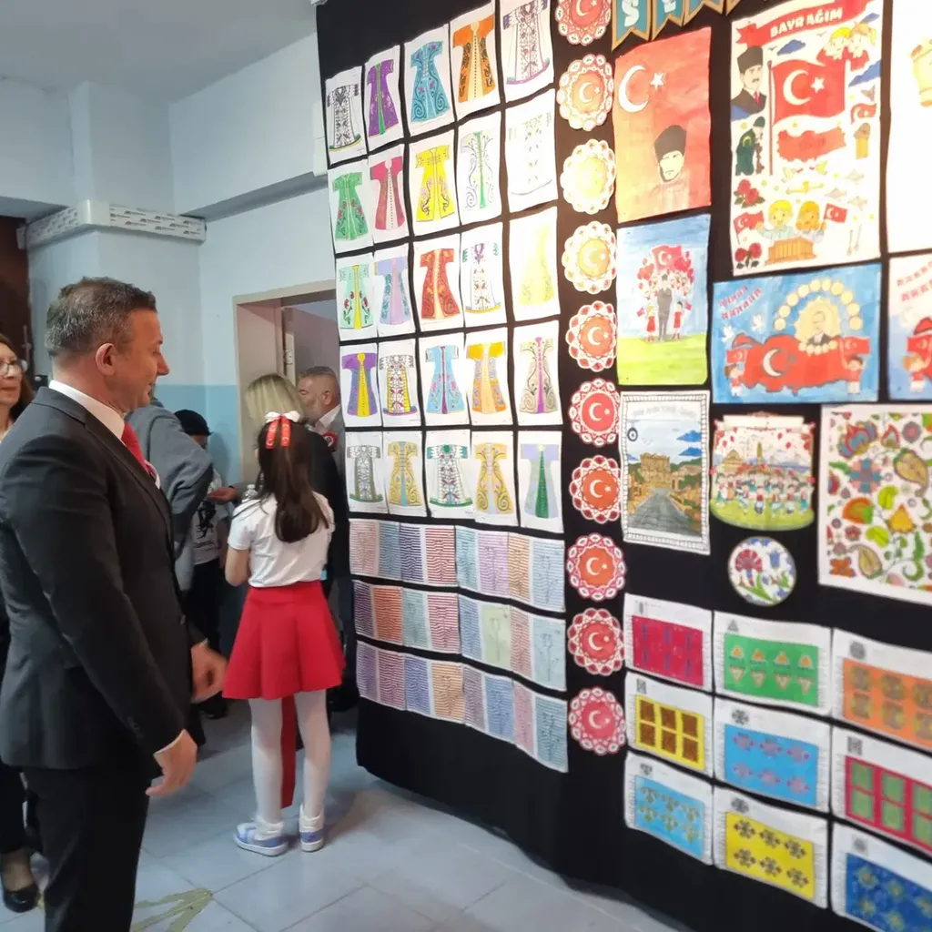 Çiğli Kaymakamı Fatih Görmüş, Turan Çakın İlkokulu'ndaki 23 Nisan sergisinde duvarlarda asılı olan öğrenci yapımı renkli kaftan resimlerini ve Türk bayrağı temalı çalışmaları inceliyor.