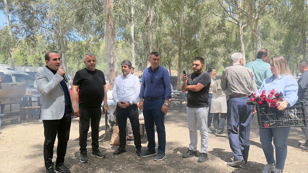 AK Parti Çiğli İlçe Başkanı Oktay Özdemir elinde mikrofonla konuşurken, yanında meclis üyesi Harbi Kurt ve teşkilat başkanı Selma Soysal yer alıyor.