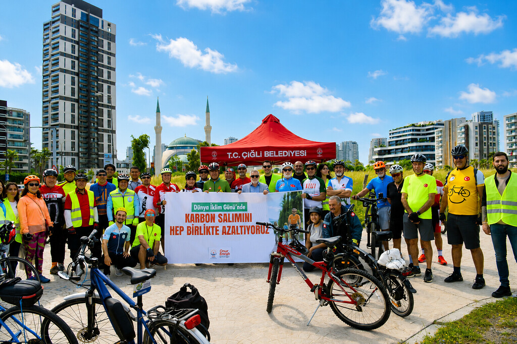Çiğli Belediye Başkanı Onur Emrah Yıldız ve bisikletlilerin "Karbon Salımını Hep Birlikte Azaltıyoruz" pankartı önünde toplu fotoğrafı.